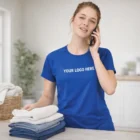 Woman in a Sols Sporty Womens T-Shirt talks on the phone while folding laundry in a bright room.