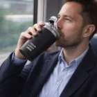 Man in suit drinks from a Swiss Peak Vacuum Cup with Your Logo Here on a train.