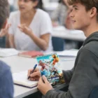 A young man takes notes in class with a Full Colour Spiral Notepads Medium in hand.