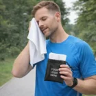 Man in blue shirt wipes face with Orleans Cooling Towels, holding branded pouch.