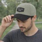 Man wearing a gray and black Braxton Caps With Patch, touching the brim outdoors.