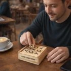 Man playing Tic Tac Toe Games on a wooden board in a café with coffee nearby.