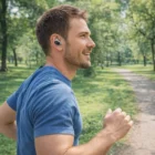 Man jogging in park, wearing blue shirt and Swiss Peak TWS Earbuds among the trees.