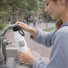Someone fills a Cheltenham Vacuum Bottle with your logo at an outdoor fountain.