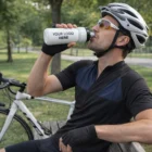 Cyclist in helmet drinks from Camelbak Podium Bike Bottle while sitting on a bench near bike.