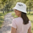 Woman in pink shirt smiling in park, wearing Manly Custom Terry Towelling Bucket Hat.