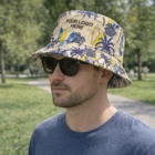 Man in sunglasses wearing a Kyler Custom Bucket Hat with "YOUR LOGO HERE," standing in a park.