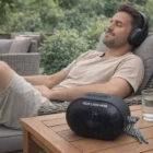 Man relaxing outdoors with Kairo headphones, near Kairo Outdoor Bluetooth Speakers.