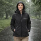 Smiling person wearing a Sols Rock Womens Softshell Jacket on a rainy park path.