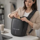 Woman puts a notebook in a Kobe Branded Sling bag with "Your Logo Here" on the front.