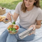 Woman outdoors eating salad on a picnic blanket with Stainless Steel Cutlery Sets.