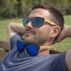 Man relaxing on a bench wearing Gideon Mirror Lens Sunglasses Bamboo, another pair on his collar.