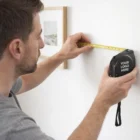 Man measures wall with Promotional Tape Measures 8M; 'Your Logo Here' shows on the tape.