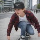 Teen boy skateboarding in city, wearing an Aziel Heather Cap and a plaid shirt.