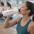 Woman hydrates with a Jarn Vacuum Bottle during yoga, bottle reads "Your Logo Here.
