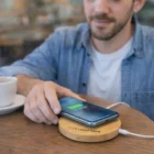 Man charging phone on Tasman Bamboo Wireless Chargers Round at cafe table with coffee cup nearby.