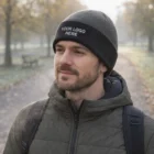 Man in park wears Kameron Two Toned Beanie with "Your Logo Here" and a green jacket.