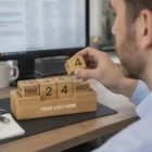 A man adjusts a Bamboo Desk Calendar by his computer, set to Wed, March 24.