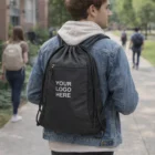 Man walking on campus with a black Aire Polyester Drawstring Bag featuring YOUR LOGO HERE.