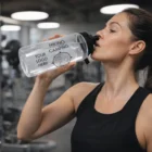 Woman in gym drinks from a clear Morgan Mountaineer Bottle labeled Hiking Camping Your Logo.