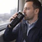 Man sipping from a Cascades Powder Coated Vacuum Tumbler, seated by a train window.