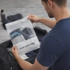 Man packing clothes into an Adelaide Drawstring Mesh Bag near a black duffel bag.