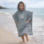 Smiling child in Hooded Towels With Pocket with Your Logo Here on a sandy beach.