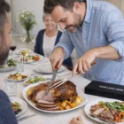 Man carves roast with Keepsake Carving Sets at a lively table surrounded by smiling guests.