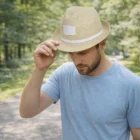 Man in a blue shirt wearing a Burnie Fedora Hat stands on a path in a green, wooded area.