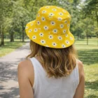Person in white tank top wearing Aero Reversible Bucket Hat with yellow daisy pattern in park.
