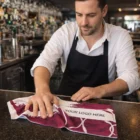 Bartender wipes bar counter with Full Colour Poly Cotton Bar Towels featuring Your Logo Here.