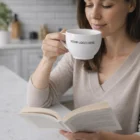 Woman reading a book and sipping from a Wheatbelt Cup And Saucers in the kitchen.