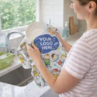 Woman dries dishes with Poly Cotton Tea Towels featuring fun cartoons and a custom logo.
