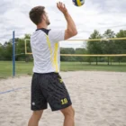 Man wearing Men's Volleyball Shorts serves on an outdoor sand volleyball court.