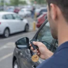 Person unlocking a car with a key fob and Santo Wooden Round Key Ring in a parking lot.