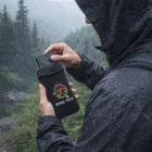 Person in rain jacket puts phone into Water Resistant Phone Pouch outdoors in the rain.