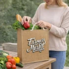 Woman placing vegetables into a Natural 30L Jute Tote Bag on an outdoor table.