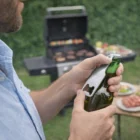 Man using a Bottle Opener Key Ring, shaped like a bottle, near a grill outdoors.