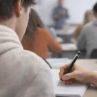 Student in class writing notes with Aluminium Guilloche Ballpoint Pen; others blurred behind.