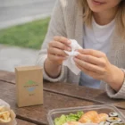 Woman uses Handy Travel Tissues while dining outdoors with sushi and fries.