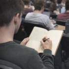Student taking notes in a Soft Kraft Cover Notebook during a busy classroom lecture.