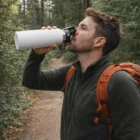 Man with a backpack drinks from a Vacuum Bottles With Carry Lid 1L on a forest trail.