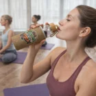 Woman drinks from a Glista Glass Bottle With Natural Sleeve during a yoga class.