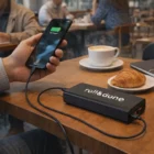 Person charging phone with a 20,000mAh Power Bank at a café table with coffee and croissant.