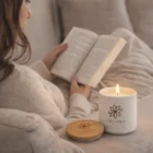 A person reads on a couch beside a lit 150G Candle With Lid in a white Organo jar.