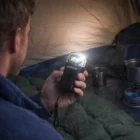 Camper inside tent holding a Solar Dynamo Torch with camping gear in the background.