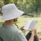 Person wearing a Premium Bucket Hat reads a book while sitting on grass in the sun.