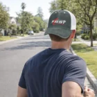 Man in Structured Trucker Cap walks down a sunny, tree-lined street.