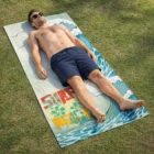 Man in sunglasses relaxes on grass with Sand-Free Soft Towel, enjoying surf-inspired vibes.