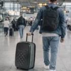 Man pulls Flex Earth Suitcases Small through airport terminal, travelers behind him.